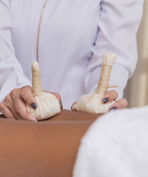 Herbal massage with pindas on the legs. Ayurveda medicine and aromatherapy treatment, anti-stress and anti-insomnia. Cotton cloth bags with herbs and medicinal plants.